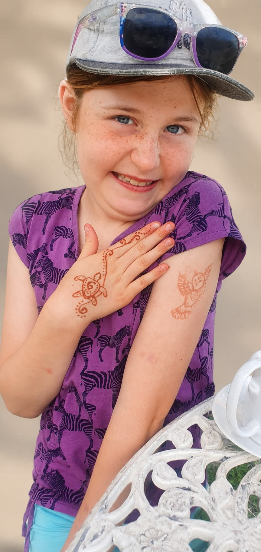 Smiling girl showing a turtle henna on her hand and an owl on her arm in warm next-day colour